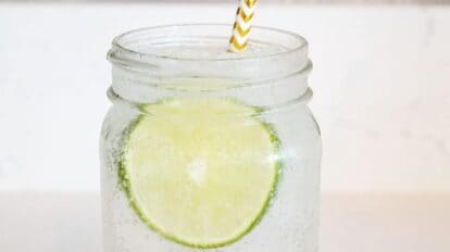 mason jar on countertop filled with vodka soda and lime slices and straw