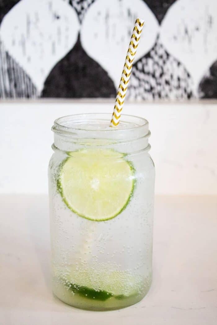 mason jar on countertop filled with vodka soda and lime slices and straw