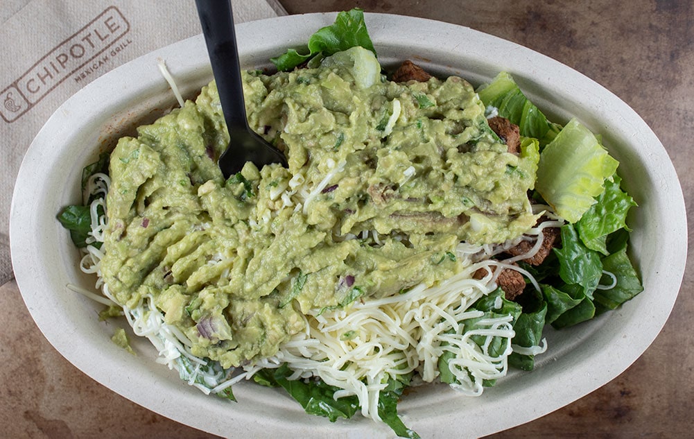 chipotle keto salad bowl covered with guacamole and a black fork sticking out of the top of the food