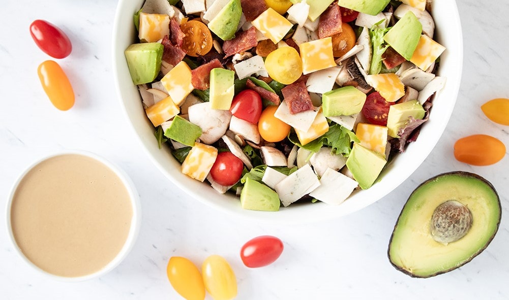 closeup of loaded keto salad surrounded by tahini and avocado