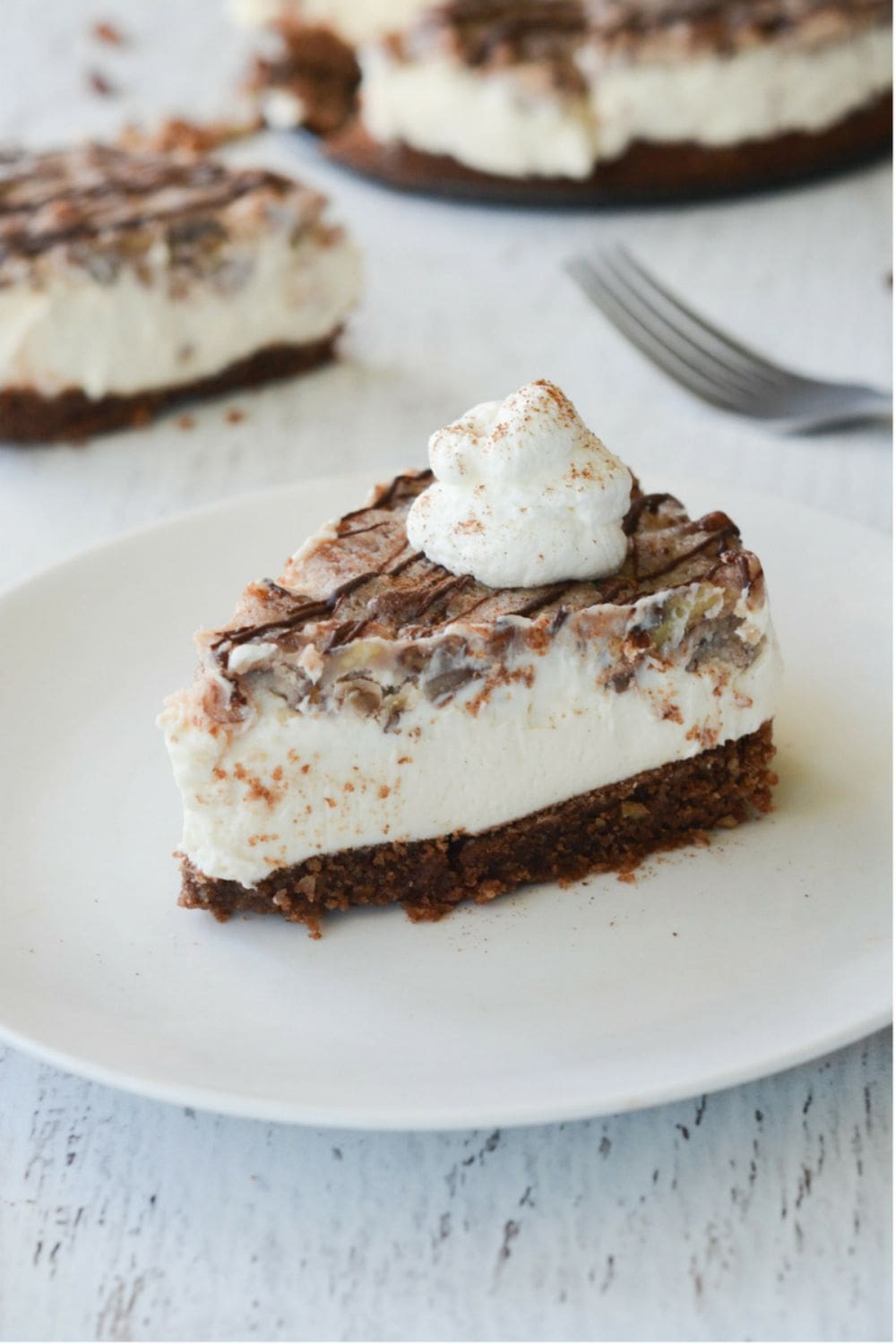 slice of pecan pie keto cheesecake sitting on a dish with pecans and whipped cream topping