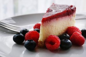 slice of keto cheesecake on a grey plate surrounded by blueberries and raspberries