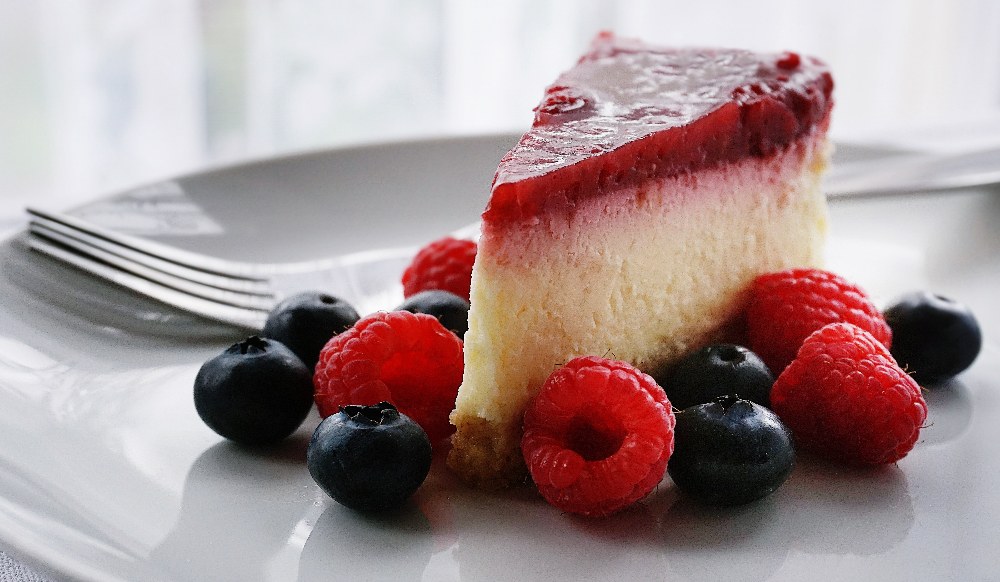 slice of keto cheesecake on a grey plate surrounded by blueberries and raspberries