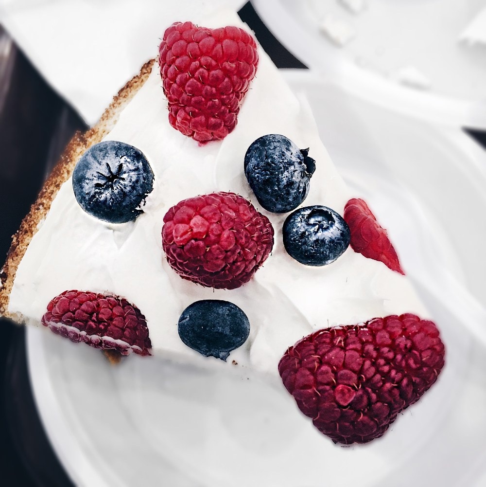 bright keto cheesecake covered with raspberries and blueberries on a white plate