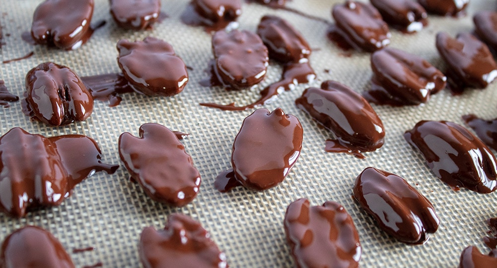 chocolate covered pecans with wet chocolate sitting on a silicone baking mat