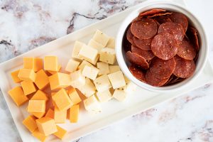 keto pepperoni in a white bowl next to two piles of cubed cheese