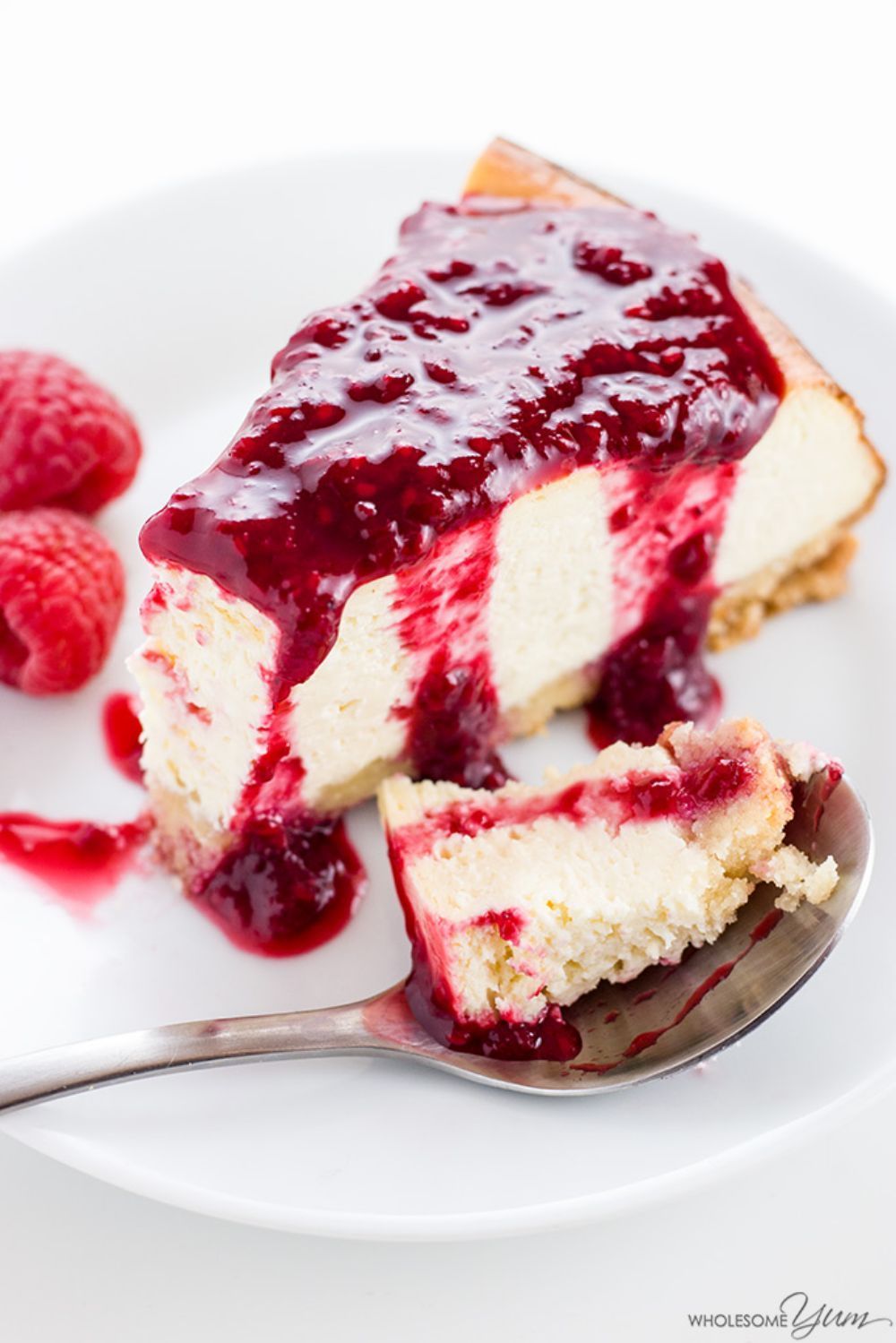 slice of New York Style keto cheesecake with raspberry topping next to a spoon