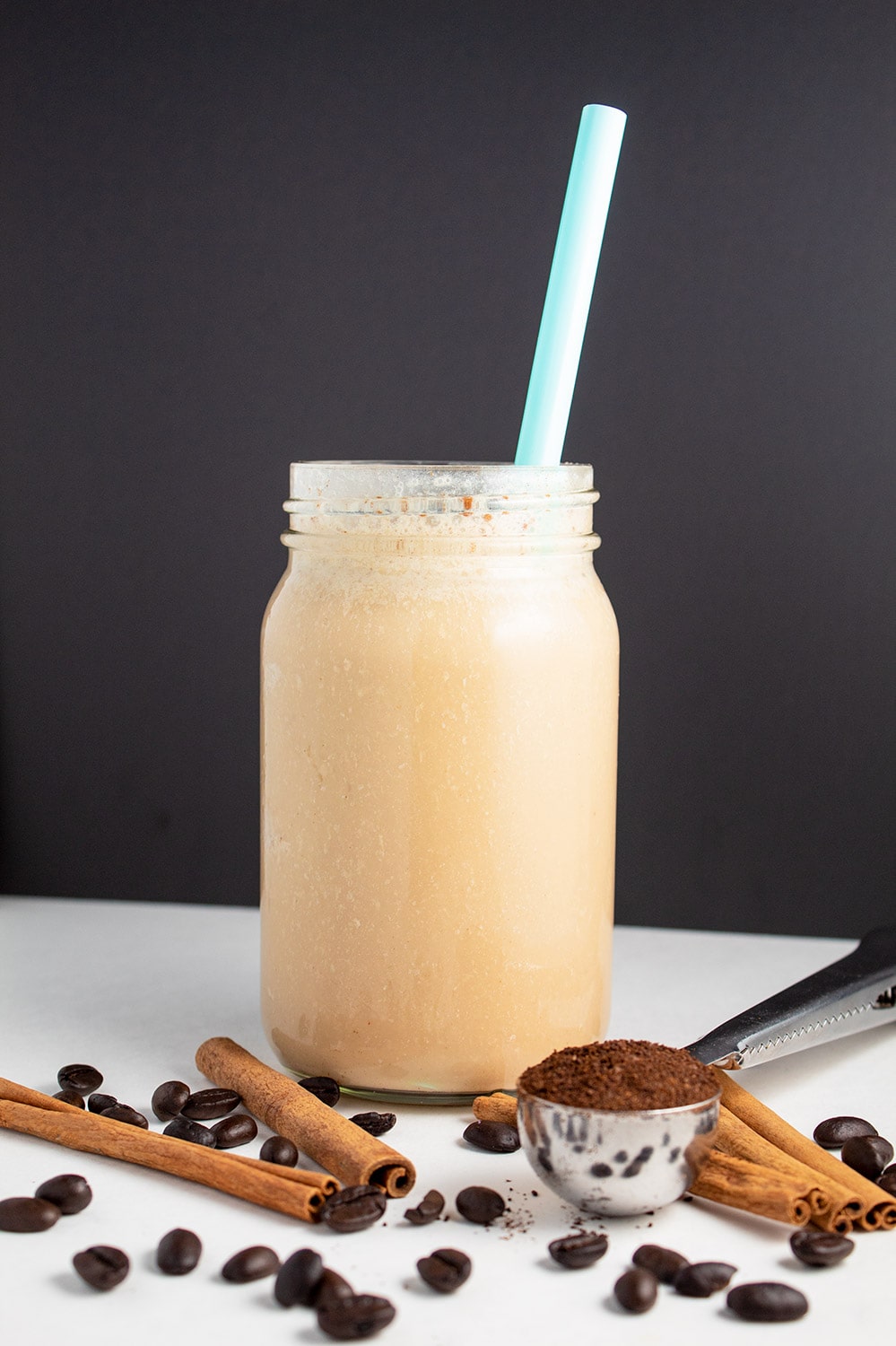 keto iced coffee with blue straw with cinnamon sticks and coffee beans on table