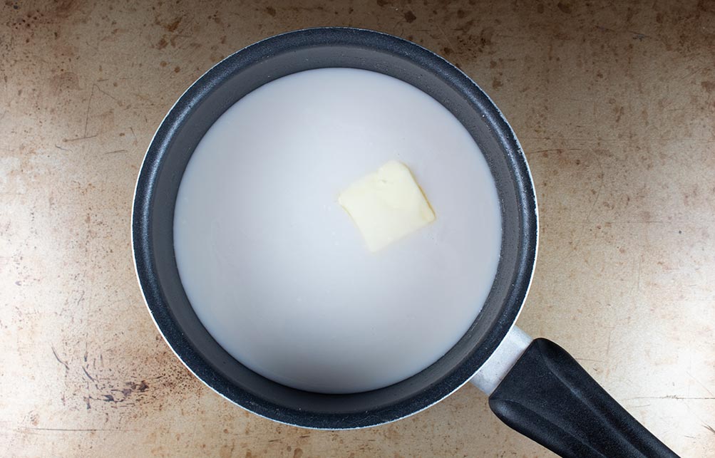 keto hot chocolate with almond milk in a sauce pan with a pat of butter