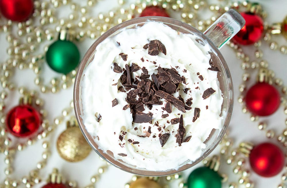 overhead horizontal view of keto starbucks peppermint mocha with red, green, and gold christmas bulbs on the ground