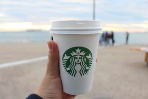 keto starbucks cup in someone's hand held out in front of a scenic beach