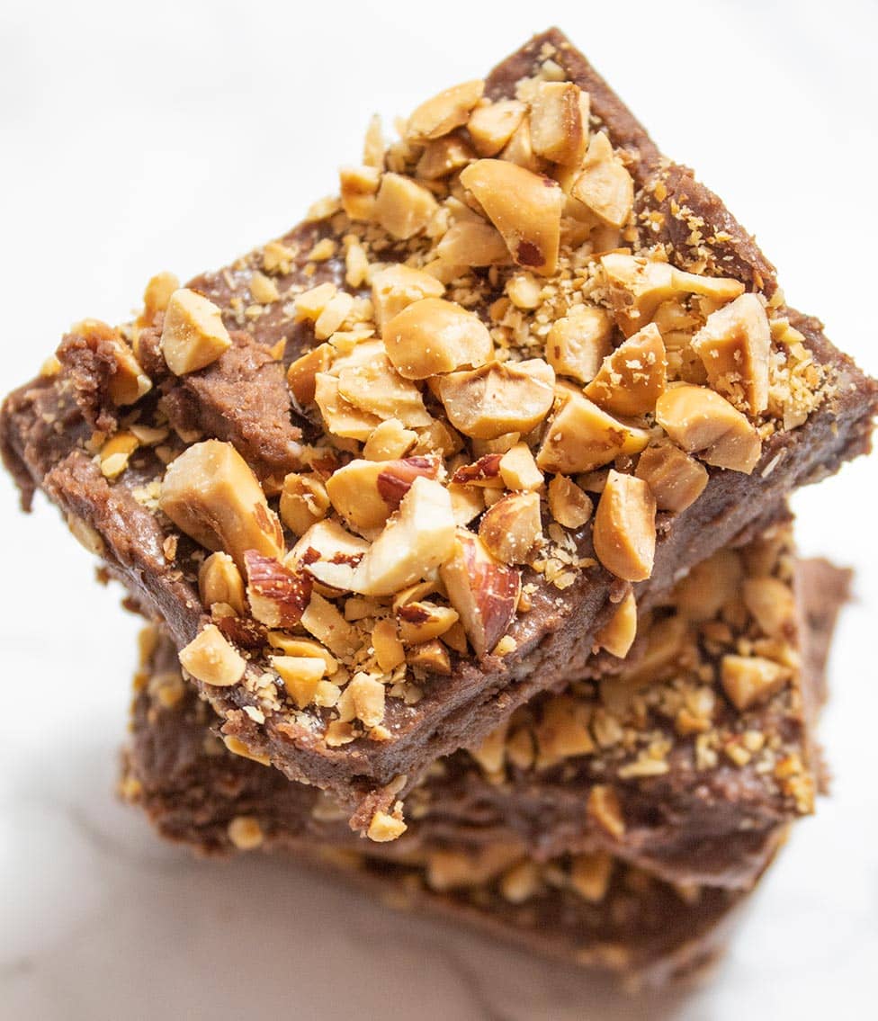 three stacked keto nutella bars on a white background with crushed hazelnuts