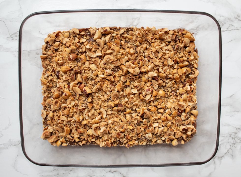 keto nutella bars in a glass baking dish covered with chopped roasted hazelnuts