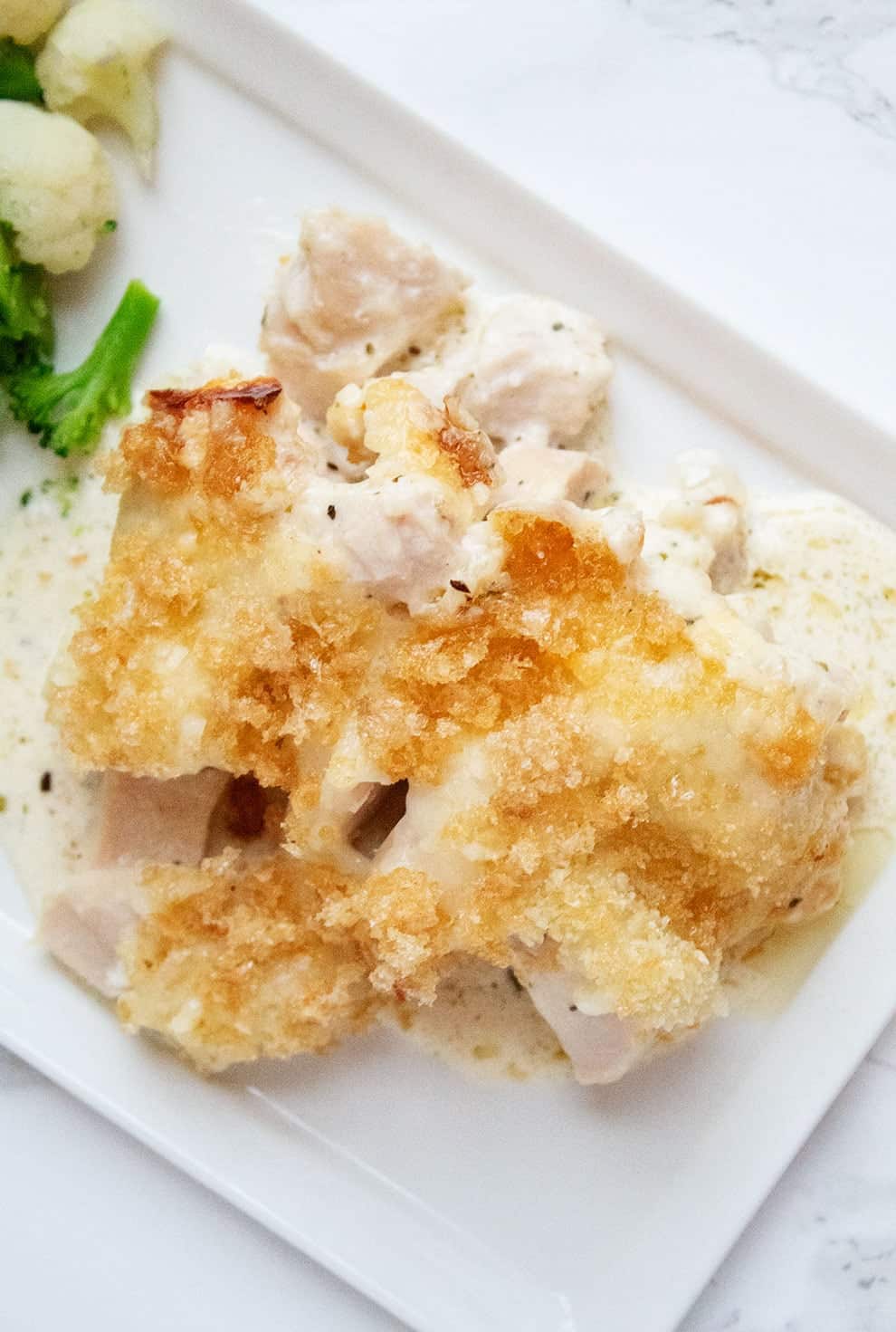 overhead view of keto chicken alfredo casserole on a white plate next to broccoli and cauliflower
