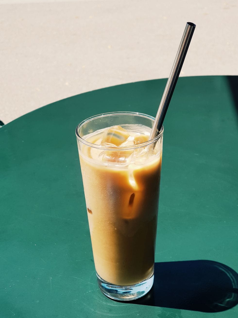 green table with keto iced coffee in a glass on top with a black straw