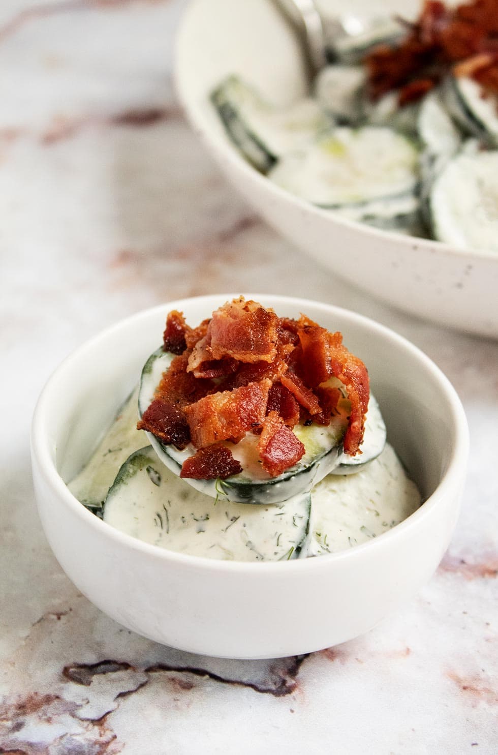 closeup view of keto cucumber salad with a slice of bacon crumbled on top