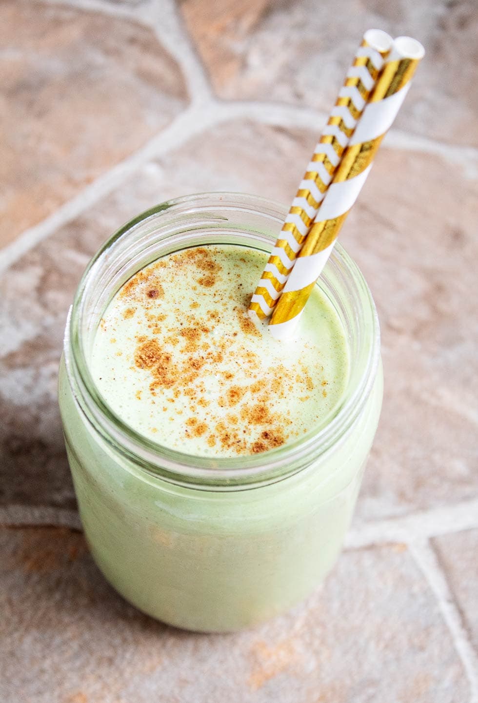 a keto green smoothie in a glass jar with two gold colorful straws sticking out on the right side