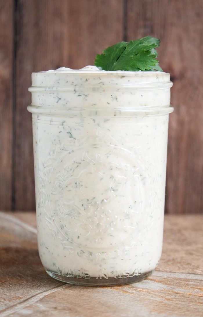 side view of mason jar filled with keto ranch dressing and a sprig of parsley on top