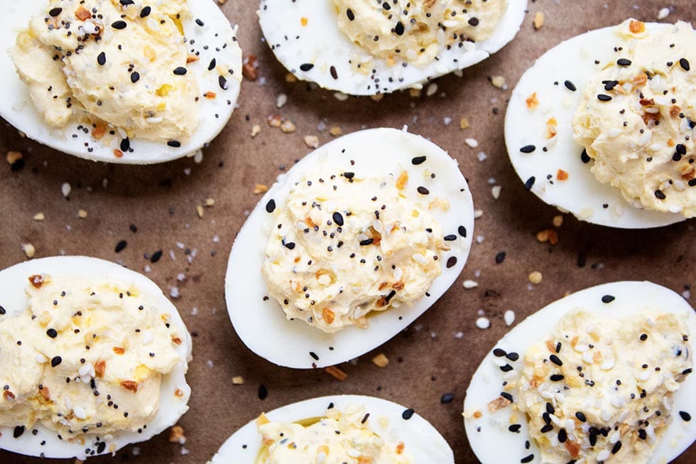 seven keto deviled eggs on a baking sheet with seasoning sprinkled on top