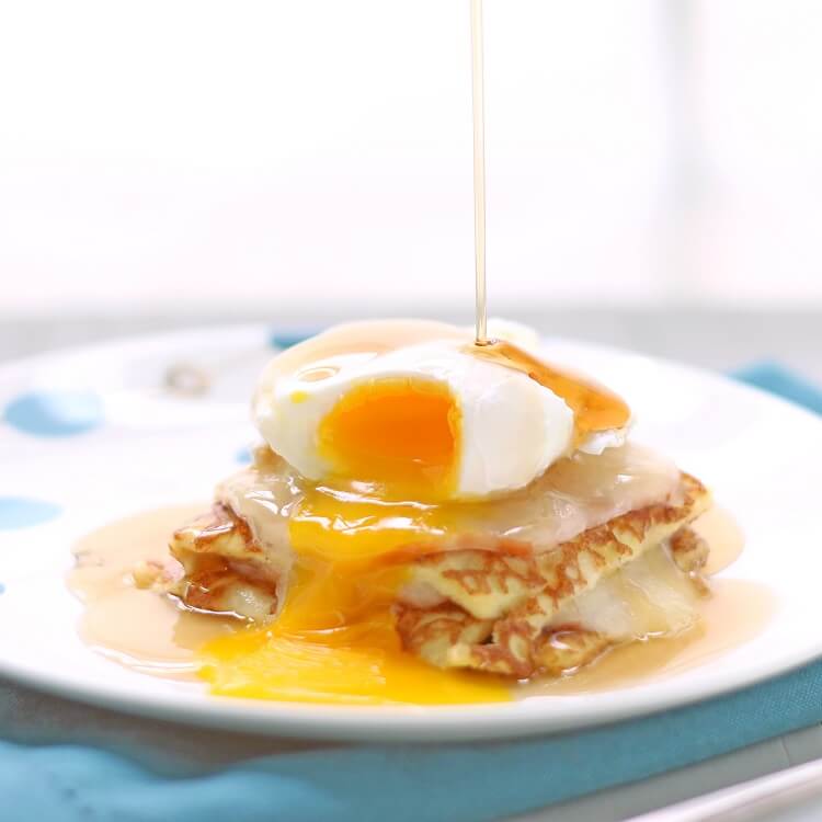 maple syrup being drizzled down on top of an egg over a slice of casserole