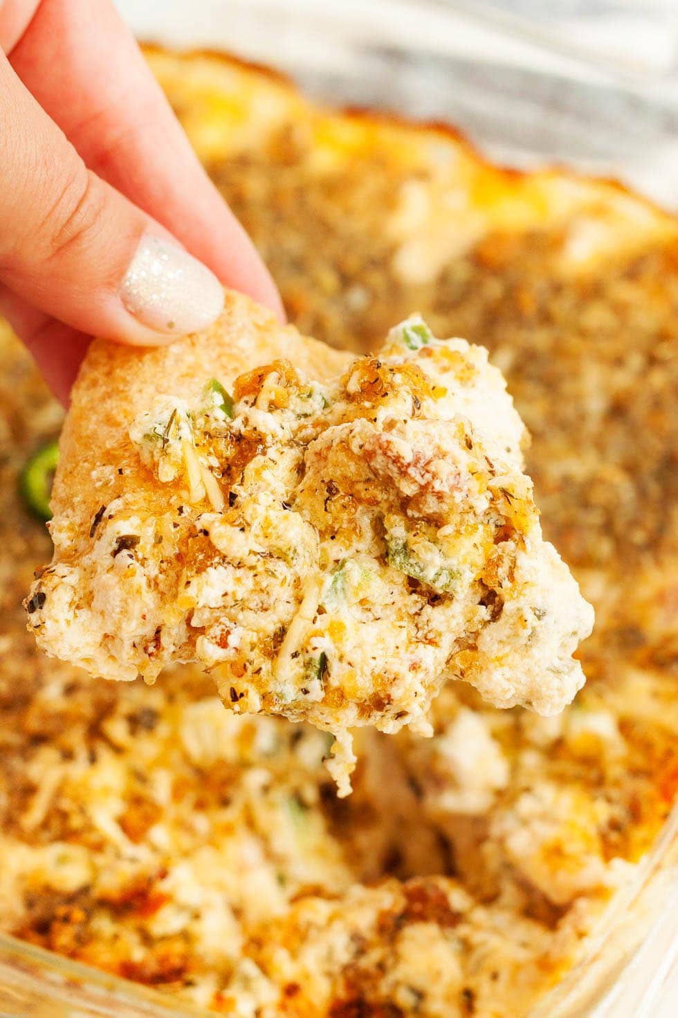 closeup of hand holding keto jalapeno popper dip over dish