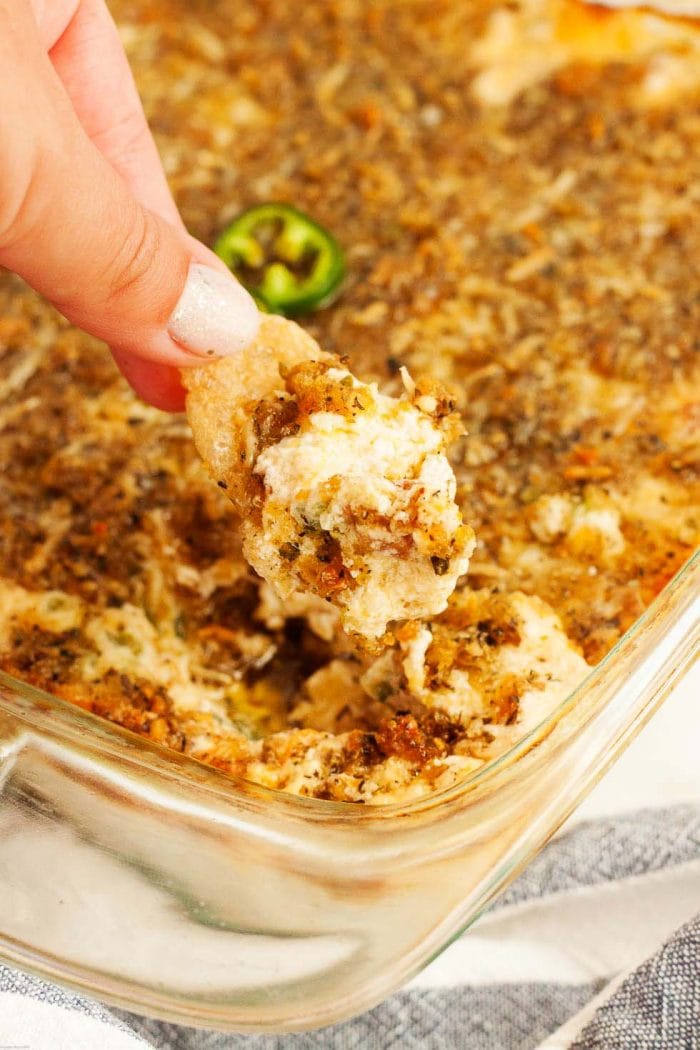 woman's hand dipping a pork rind into keto jalapeno popper dip