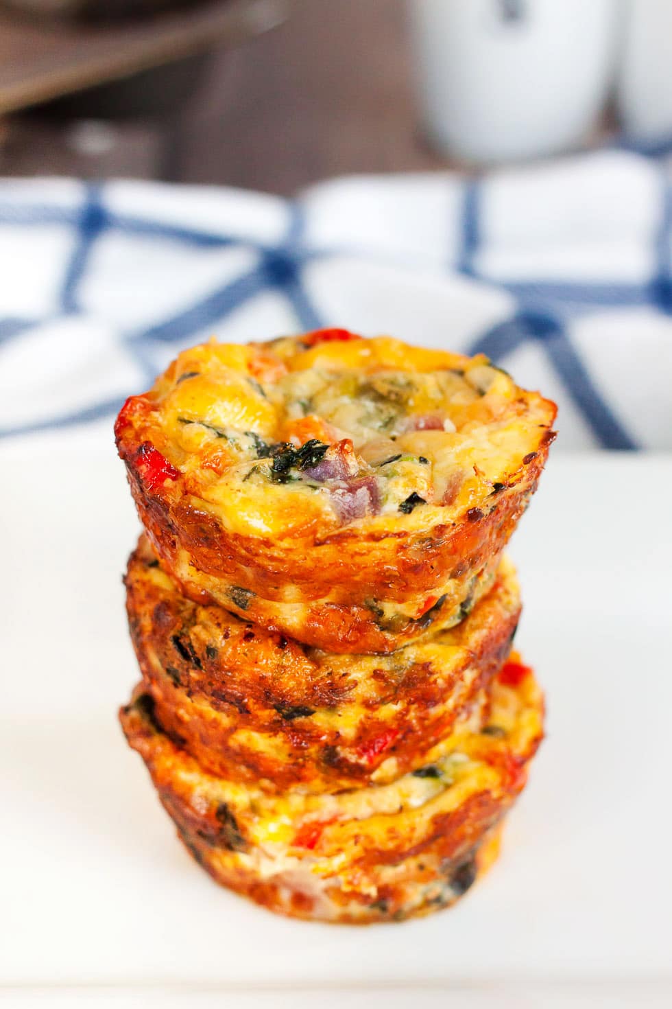 four keto mini quiches stacked high on a white plate next to a blue and white towel