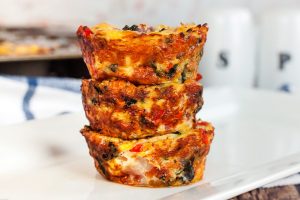 three keto mini quiches stacked high on a plate next to a salt and pepper shaker