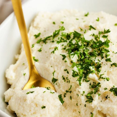 closeup of gold spoon inside keto mashed cauliflower with parsley on top