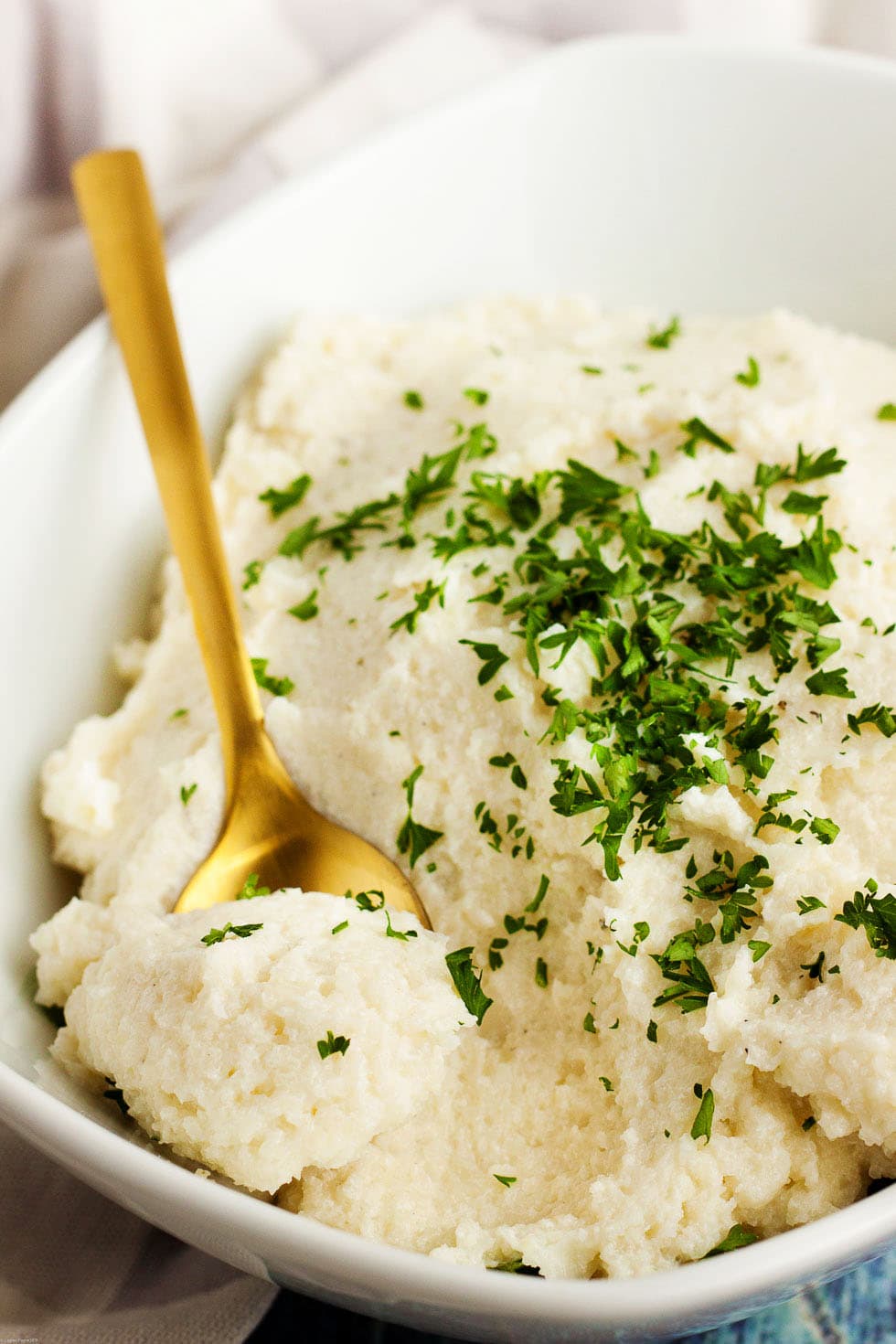 closeup of gold spoon inside keto mashed cauliflower with parsley on top