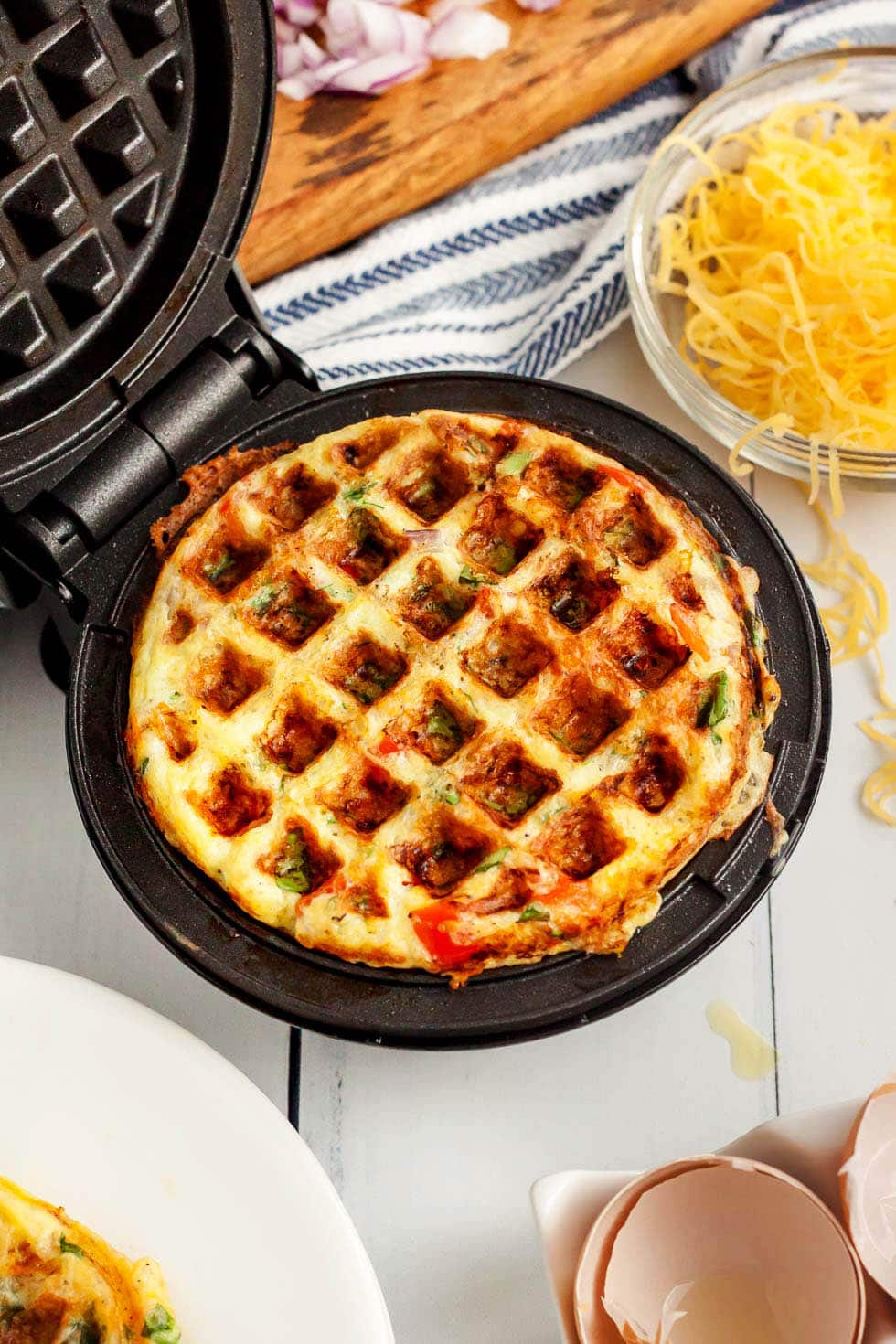 keto chaffle omelet in a mini waffle maker next to a container of cheese