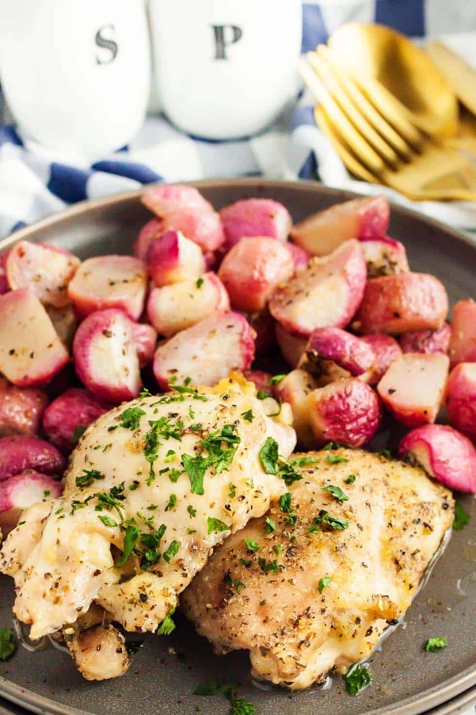 sheet pan chicken thighs sitting on a large plate next to roasted radishes and gold silverware