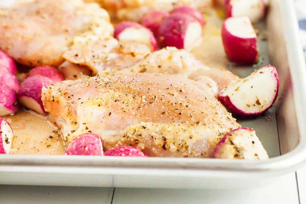 close up of chicken thighs with radishes on pan before cooking