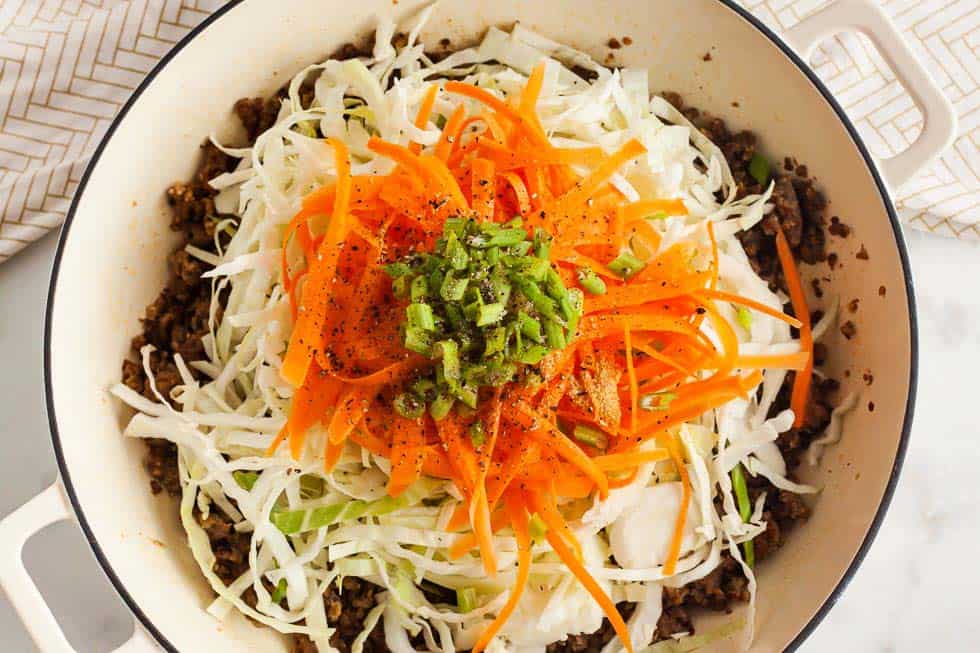 shredded carrots and shredded cabbage on top of cooked pork sausage in a bowl