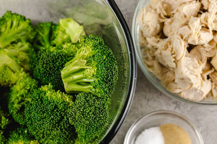 overhead view of broccoli, chicken breast, and spices in bowls