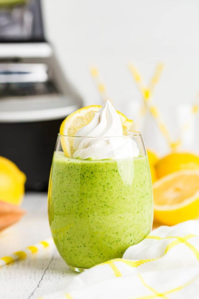 keto lemon pie smoothie in a glass in front of a blender and sliced lemons
