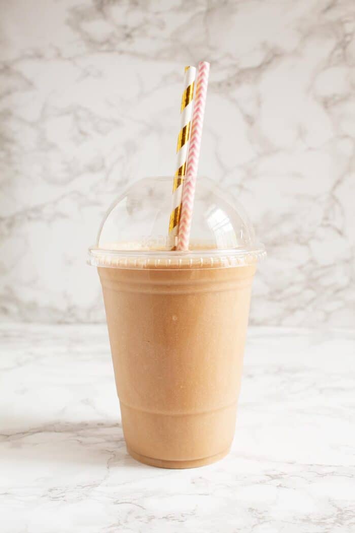 keto frappuccino in a plastic cup with two decorative straws in front of marble