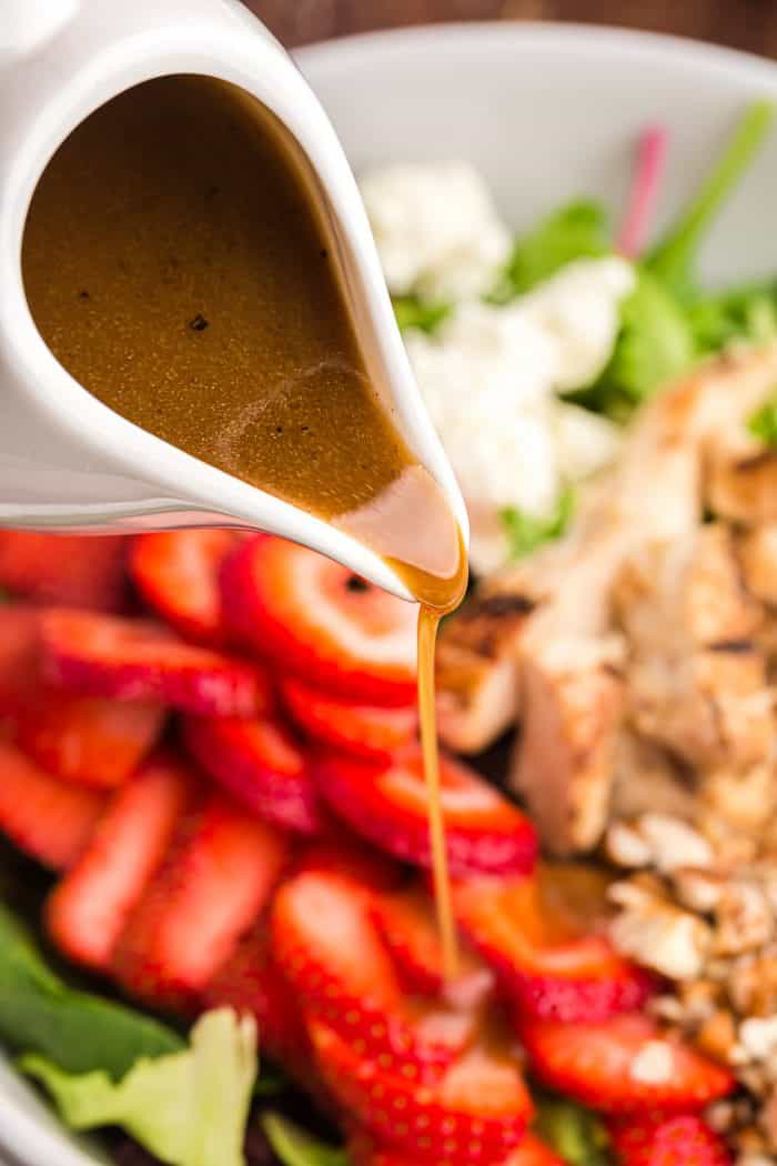 white cup pouring keto salad dressing onto keto chicken salad with strawberries