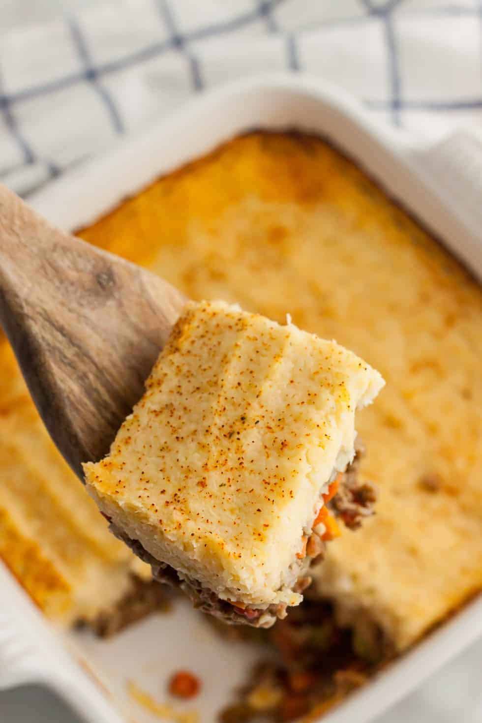 spoon holding up slice of keto shepherd's pie above a casserole dish