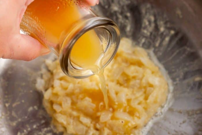 chicken broth being poured into buttery onions
