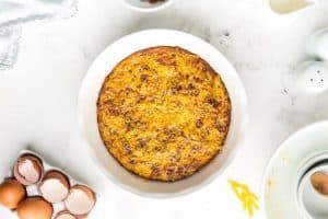baked low carb quiche in a white pie pan next to broken eggs