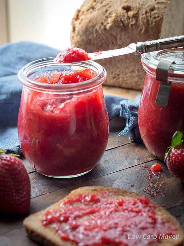 glass jar of keto strawberry jam next to a piece of jam-covered keto bread