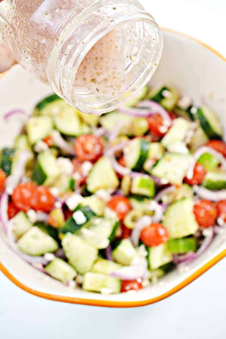 greek keto salad dressing being poured into greek salad in a bowl