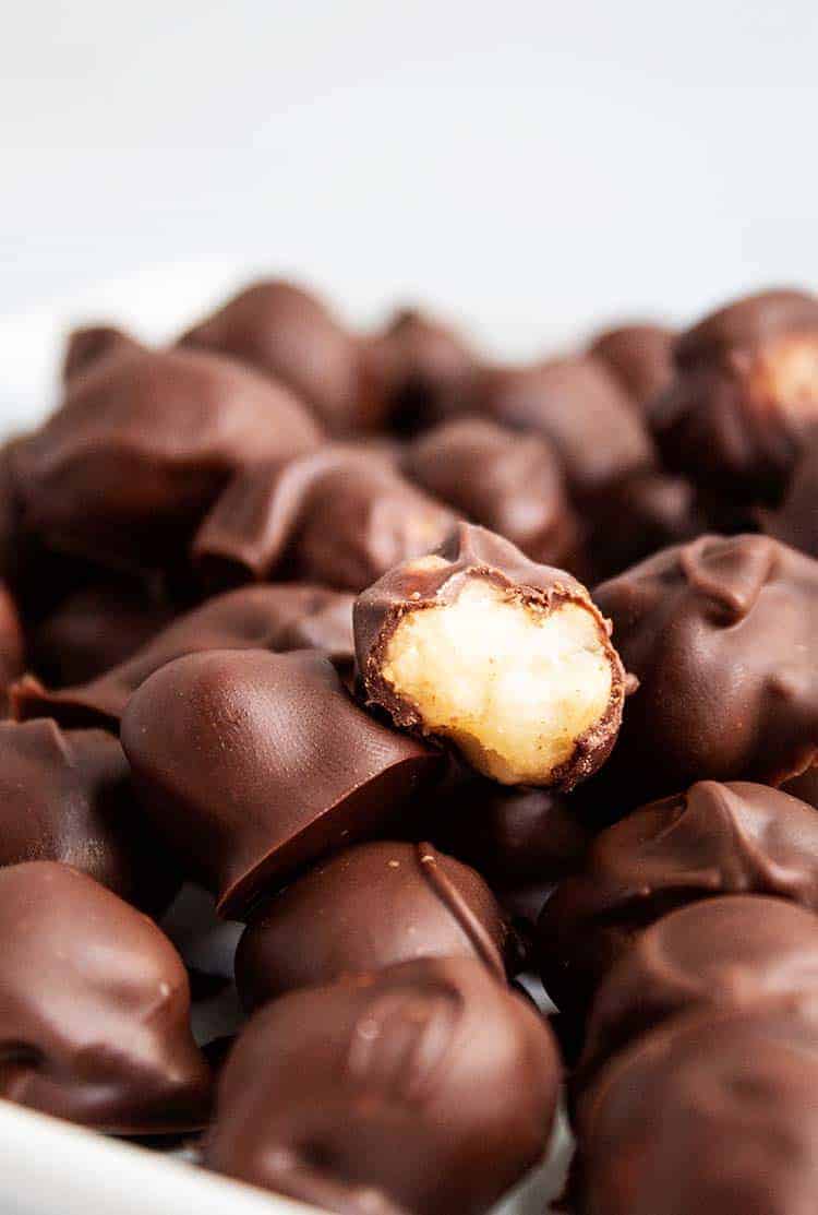 closeup of half-eaten chocolate covered macadamia nut in a bowlful of macadamia nuts