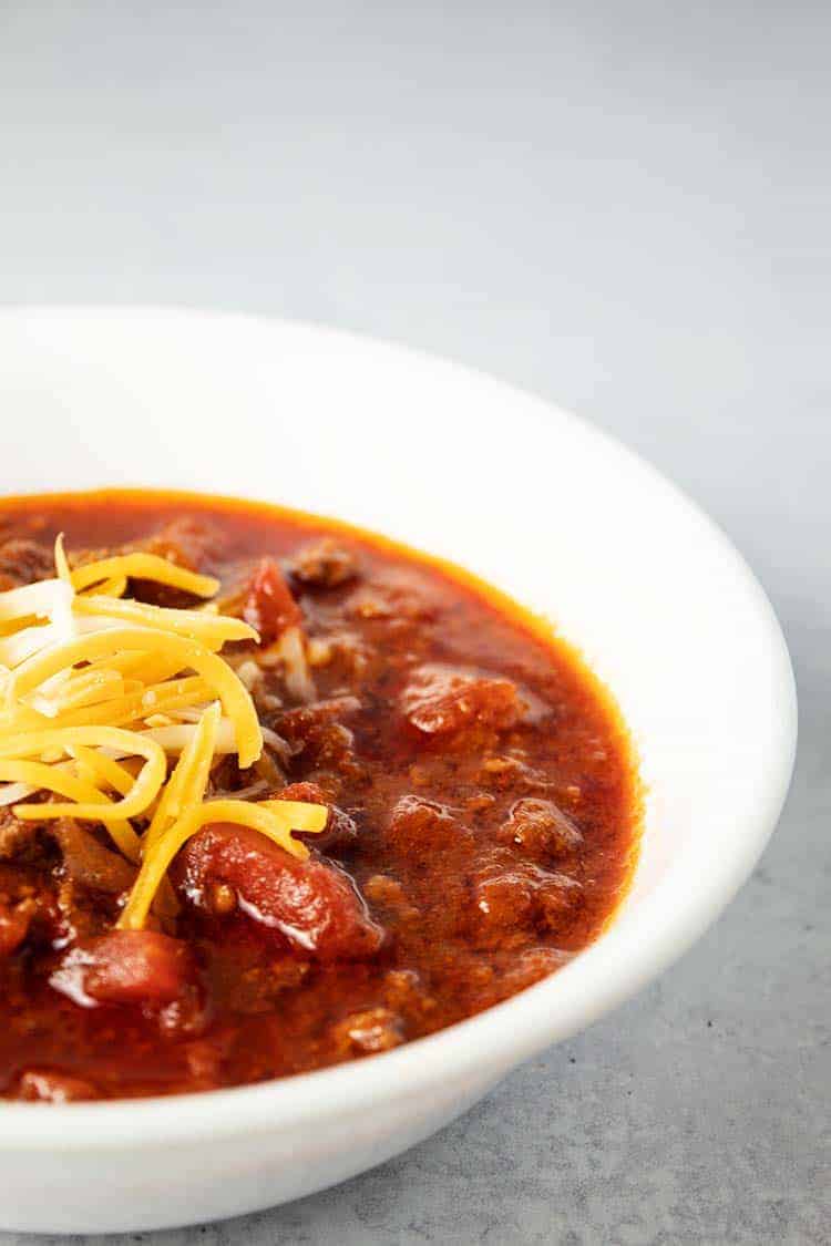 side view of white bowl containing keto chili topped with cheese