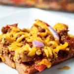 piece of keto chili dog casserole on a white plate with casserole dish in background