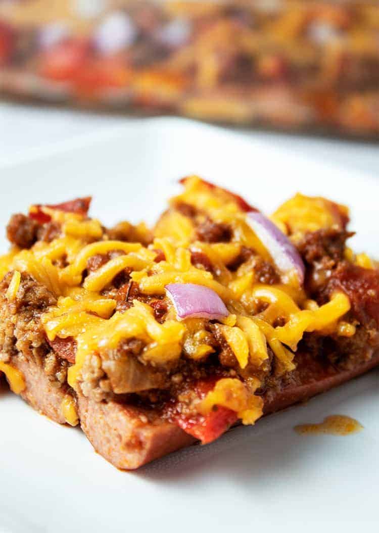 piece of keto chili dog casserole on a white plate with casserole dish in background