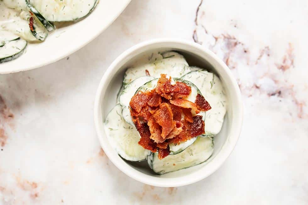 overhead view of small white bowl containing keto cucumber salad next to a larger bowl with cucumber salad