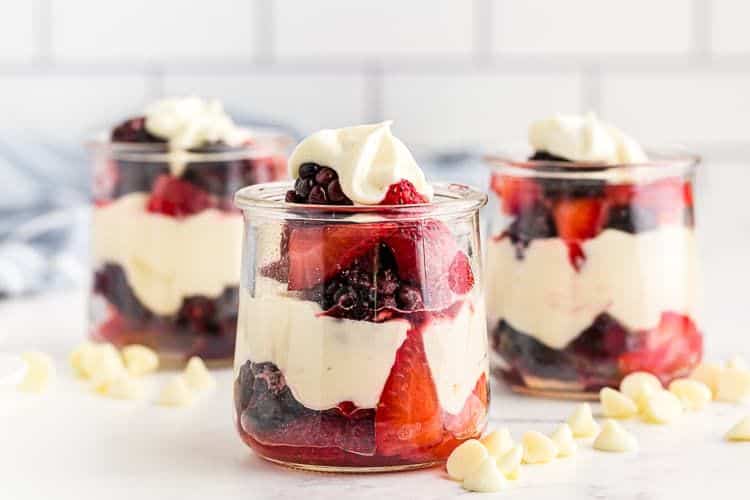 closeup view of three glass jars containing white chocolate mousse layered with berries