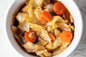 keto cabbage soup in a small white bowl with chopped carrots on top